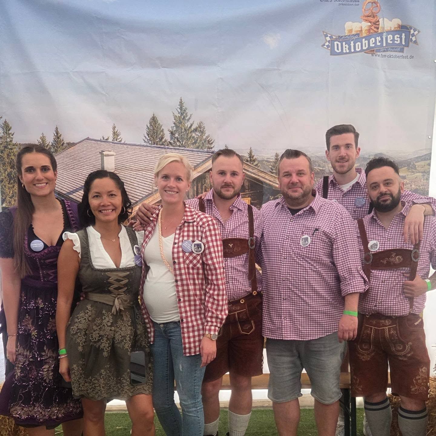 Mitglieder in Dirndl und Lederhosen vor der Oktoberfest-Kulisse